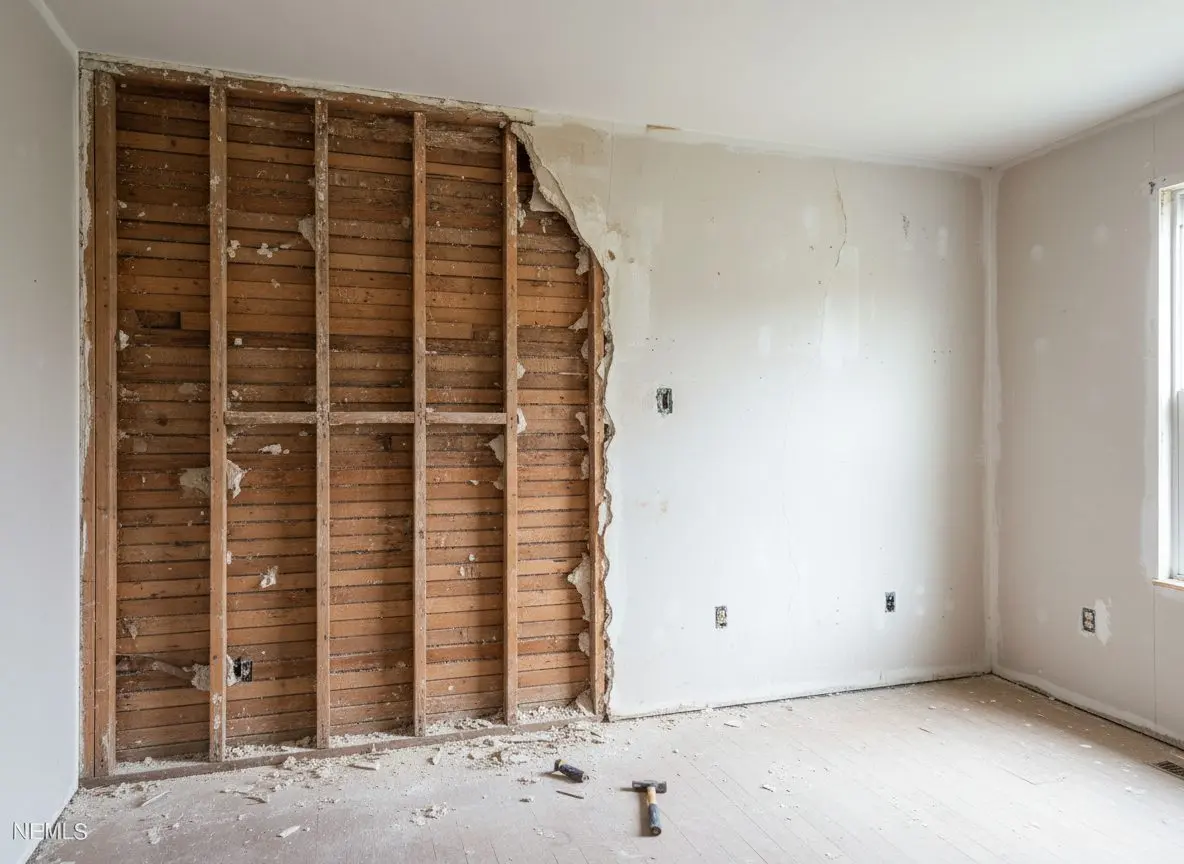 A wall part way through being opened, old plaster and wood lath stripped from the left half and bare studs showing